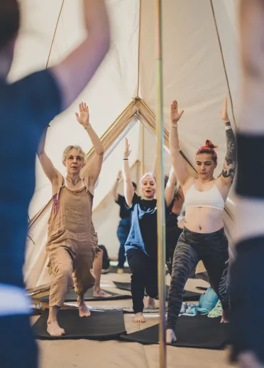 Un groupe de womxn faisant du yoga sous une tente de festival