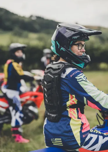 Une personne portant un casque et des équipements de sécurité pour la moto, tenant une moto et souriant