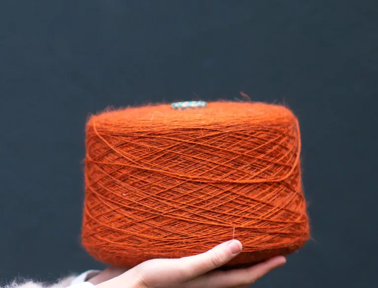 Une main tenant une grande bobine de laine orange.
